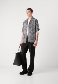 Short-sleeve black and white patterned shirt, white t-shirt underneath, black trousers, black tote bag, and black shoes. Smooth textures.