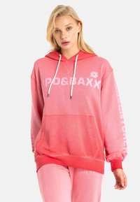Pinker Farbverlauf-Hoodie mit weißem Text auf der Vorder- und der Ärmelseite, ausgestattet mit einer Kängurutasche und einer Kapuze mit Zugkordel. Aus einem Baumwollgemisch.