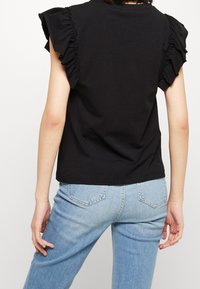 Zwart katoenen T-shirt met rimpelige korte mouwen, ronde halslijn en een losse pasvorm. Gepaard met lichtblauwe denim jeans.