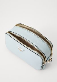 Light blue faux leather bag with dual zippers, gold hardware, and a textured finish. Rounded rectangular shape with a logo accent.