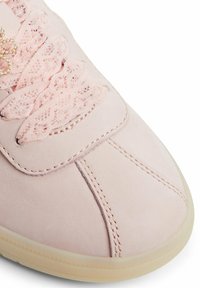Sneaker rosa in pelle con dettagli in pizzo sulla linguetta, accenti cuciti e suola in gomma di colore chiaro.
