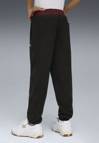Sorte sweatpants med en maroon talje, med sidelommer og slim fit, parret med hvide sneakers. Puma-logo detaljer synlige.