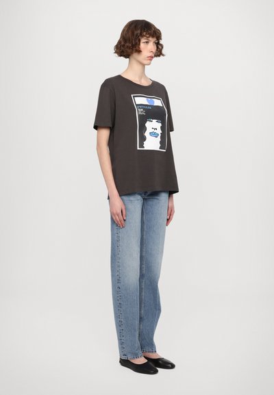 Mørk grå t-skjorte med grafisk trykk av et ansikt med blå detaljer, kombinert med lyseblå straight-leg jeans og svarte flate sko.