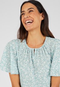 Lichtblauwe bloempat blouse met korte vlindermouwen, met een geraffineerde halslijn en een sleufopening aan de voorkant.