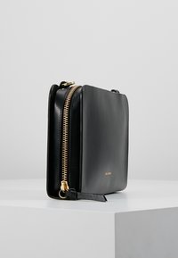 Borsa in pelle nera con forma rettangolare, zip dorata e dettaglio del logo in rilievo. Texture liscia e design minimale.
