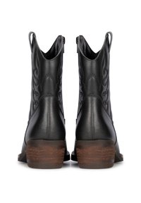 Botas de tobillo de cuero negro con un diseño texturizado, cremalleras y un tacón de madera apilada. Parte superior lisa con detalles de costura distintivos.