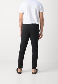 Pantaloni neri su misura con una vestibilità slim, realizzati in un tessuto liscio. Presentano un orlo arrotolato e due tasche posteriori. Indossati con una maglietta bianca.