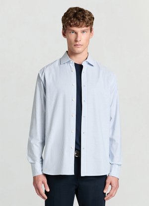 Chemise à rayures bleu clair avec col boutonné, manches longues et détails subtils au niveau des poignets, associée à un haut bleu marine foncé en dessous.