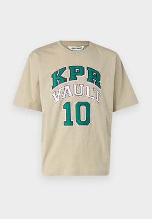 T-shirt en coton beige à manches courtes, présentant un grand graphique "KPR VAULT 10" en vert et blanc. Texture douce et coupe décontractée.