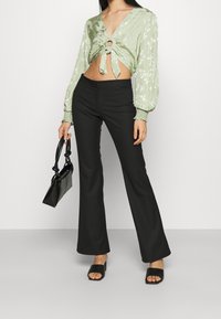 Lys grøn blomsterprint crop top med bånd foran, parret med sorte flagrende bukser og åbne sorte slide sandaler, mens der bæres en sort handbag.
