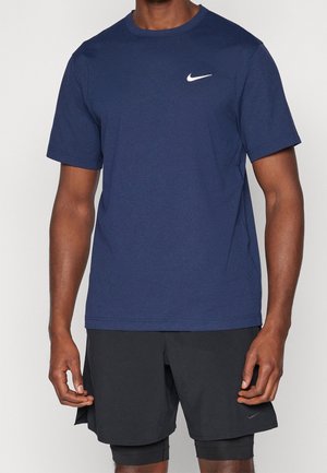 Mand iført en mørkeblå Nike T-shirt og sorte Nike-shorts med indbyggede kompressionsleggings, stående med afslappede arme.