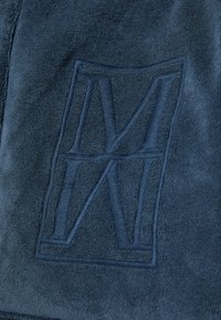 Navy blue towel with a textured finish, featuring an embossed logo in the shape of the letters M and N. Soft, absorbent material.