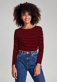 Top a maniche lunghe a righe rosse e nere con scollo rotondo, abbinato a jeans blu a vita alta. Tessuto liscio con un taglio aderente.