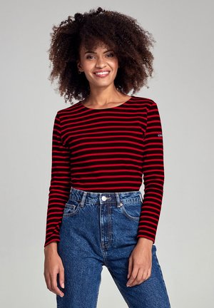 Top a maniche lunghe a righe rosse e nere con scollo rotondo, abbinato a jeans blu a vita alta. Tessuto liscio con un taglio aderente.