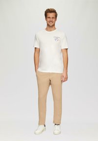 Korte mouwen crèmekleurig T-shirt met grafische print, gecombineerd met lichtbeige broek en witte sneakers. Eenvoudig ontwerp, casual fit en een zachte textuur.