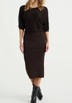 Femme portant une tenue deux pièces marron foncé scintillante avec une jupe midi ajustée et un top à manches trois-quarts, associée à des bottines noires.
