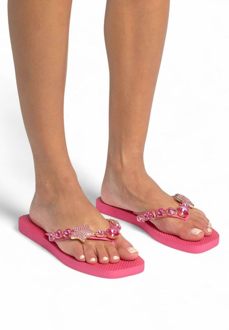 Chanclas rosas con suela texturizada y una correa decorativa adornada con gemas rosas y un acento en forma de estrella. Diseño simple con estilo casual.