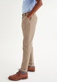 Beige Hosen mit geradem Schnitt und Seitentaschen, kombiniert mit braunen Brogue-Schuhen mit perforierten Details und gemusterten Socken.
