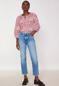 Blusa a maniche lunghe con un motivo paisley rosa e crema, abbinata a jeans dritti azzurri e mocassini scuri.