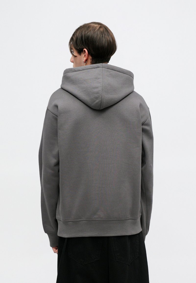 Grauer Kapuzenpullover mit lockerer Passform. Weicher Stoff, gerippte Bündchen und Saum. Keine sichtbaren Logos oder Muster. Getragen mit schwarzen Hosen.