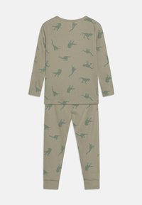Ensemble pyjama en tissu côtelé vert pâle présentant diverses silhouettes de dinosaures et de lions en vert plus foncé. Manches longues et pantalon avec poignets.