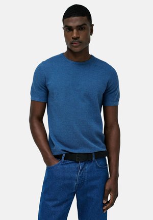 Camiseta de punto azul de manga corta con cuello redondo, combinada con unos vaqueros de mezclilla azul oscuro y un cinturón negro, con una textura suave.