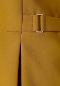 Gros plan sur un tissu jaune moutarde avec une couture cousue et une boucle de ceinture avec une boucle métallique rectangulaire sur un vêtement.