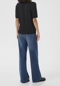 Haut noir à manches courtes associé à un jean en denim bleu à la coupe ample, jambes droites et coutures discrètes sur les poches arrière.