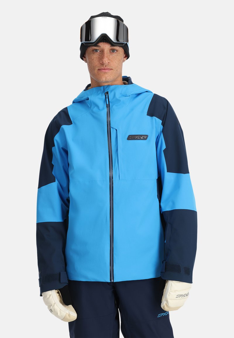 Blau und marineblaue Skijacke mit einem Reißverschluss vorne, verstellbare Kapuze und Logo auf der Brust. Sie verfügt über elastische Bündchen und ein kontrastierendes Paneeldesign.