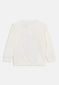 Camisola de manga longa de cor crema, feita de um tecido suave, com decote redondo, fileira de três botões nas costas e punhos canelados.