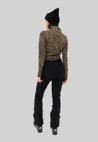 Haut à manches longues à motif léopard associé à un pantalon de ski noir et des bottes noires. Le modèle porte un bonnet en tricot noir, mettant en valeur une silhouette ajustée.
