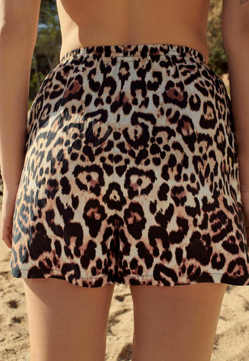 Personne portant un short en imprimé léopard se tenant à l'ext�érieur sur un sol sablonneux avec des arbres en arrière-plan.