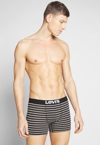 Bóxer para hombre a rayas en blanco y negro con una cinturilla de marca, que presenta una tela suave y elástica y un diseño ajustado.
