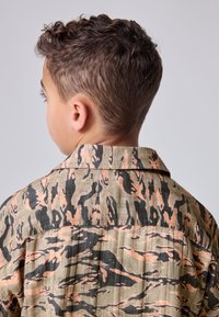 Korte mouwen, overhemd met kraag in een camouflagepatroon, met aardetinten van groen, zwart en lichtoranje en een gebreide stof.