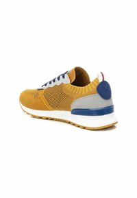 Zapatilla deportiva amarilla y gris con parte superior de malla, cordones azul marino, pestaña en el talón y suela blanca. Presenta acentos texturizados y un diseño en contraste.