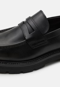 Juodi odiniai bateliai loafer stiliaus su siuvinėta detale, pakelta diržele per bato viršų ir tvirtu guminiu padu. Glotni tekstūra ir minimalistinis dizainas.