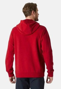 Sudadera con capucha roja de corte relajado, que cuenta con un bolsillo tipo canguro, puños y bajo acanalados. Textura suave, diseño liso.