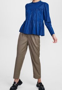 Top blu plettato a maniche lunghe con collo alto, abbinato a pantaloni a quadri chiari e mocassini neri, che mette in evidenza le texture sovrapposte.