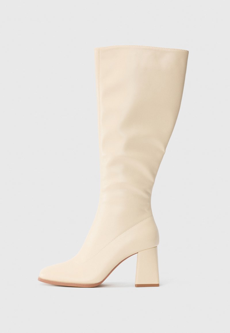 Cream-colored knee-high boot with block heel and smooth finish, shown in side profile on a plain background.