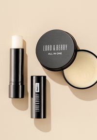 Svart cylindrisk läppbalsam, svart rund behållare märkt "LORD & BERRY ALL IN ONE," krämig lätt produkt inuti, slät textur.