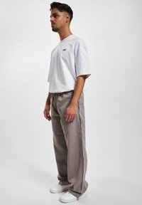 Hvid bomulds t-shirt med diskret tekst, parret med lysegrå bukser med sidelister. Modellen bærer hvide sneakers. Enkel, moderne design.