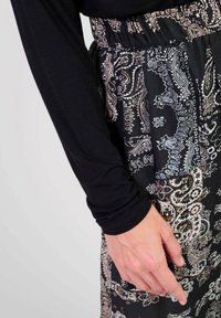Haut noir à manches longues associé à une jupe à motifs présentant un design paisley en noir, crème et marron. Taille élastique.