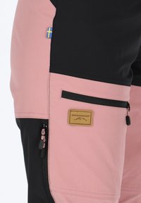 Swedemount pants featuring a color-block design with pink and black sections, zippered pockets, and a rectangular brand label.