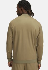 Chaqueta verde oliva hecha de una tela suave, con cuello alto, puños acanalados y un logo minimalista en la parte posterior.
