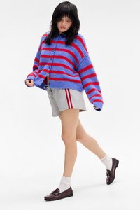 Πλεχτό σακάκι με μοβ και κόκκινες ρίγες, κουμπωμένο, πάνω από γκρι σορτς με κόκκινες πλαϊνές ρίγες και σκούρες loafers. Μαλακή υφή, χαλαρή εφαρμογή.