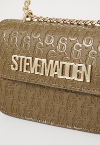 Brun mønstret crossover-veske med en pyntelærred-finish, med en gull "STEVE MADDEN" logo og en kjede-stropp. Teksturerte overflatedetaljer.