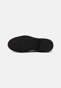 Black rubber shoe sole with a textured surface, featuring a rounded shape and a slight heel contour, showing tread patterns for grip.