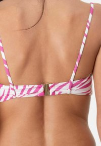 Top bikini a strisce rosa e bianche, con una chiusura dorata sul retro. Le bretelle sono sottili e regolabili, il tessuto sembra liscio.