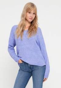 Lys lilla strikkegenser med avslappet passform, lange ermer og ribbestruktur, sammen med blå denim jeans.