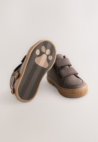 Graue Schuhe mit zwei Klettverschlüssen, profilierte Gummisohle mit Pfotenabdruck und abgerundetem Vorderteil. Weiches Material mit geriffelten Akzenten.